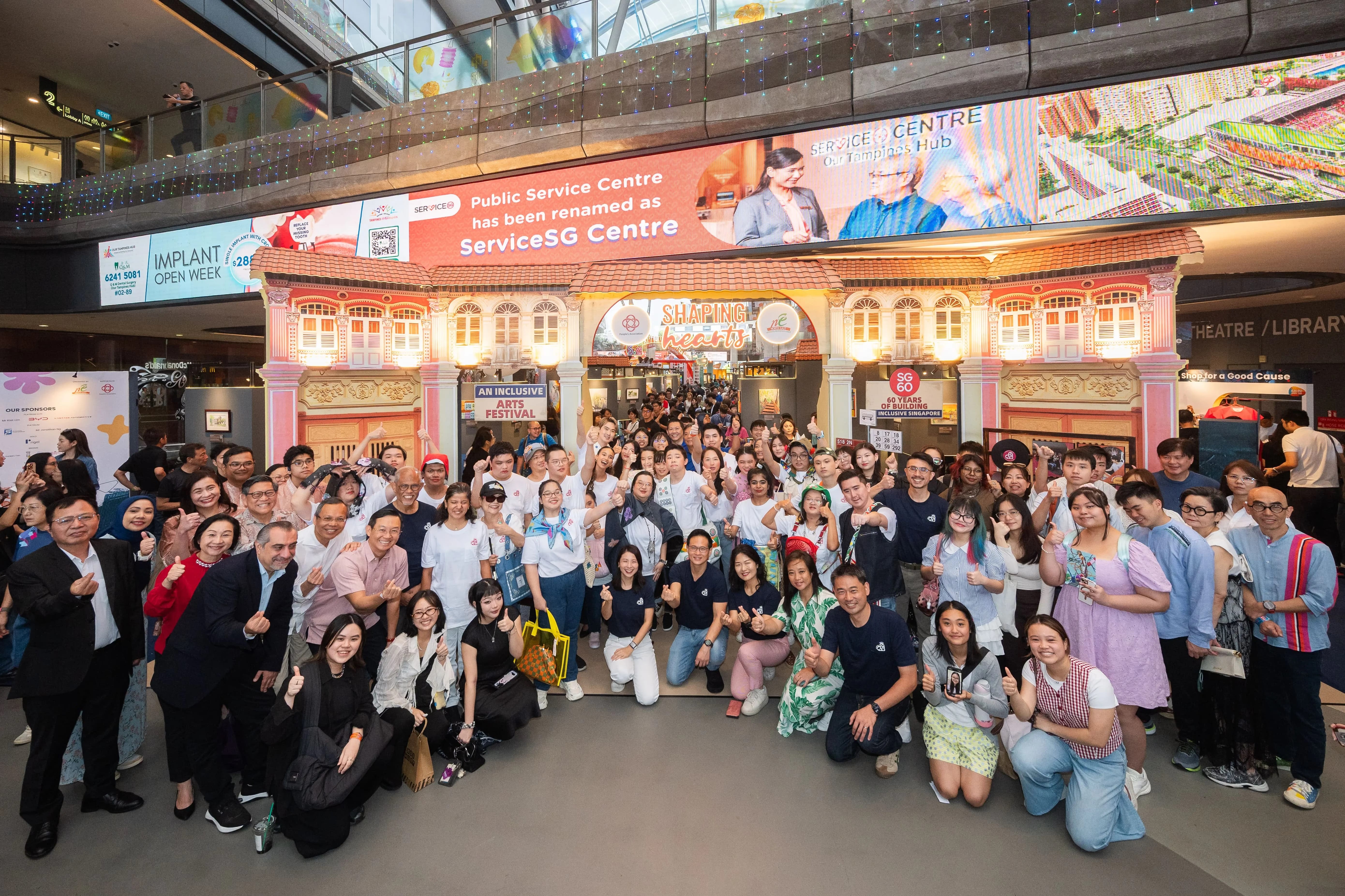 Large group photo of Shaping Hearts artists, grassroots advisors, sponsors and partners, and Temasek Polytechnic students in front of the Shaping Hearts exhibition entrance.